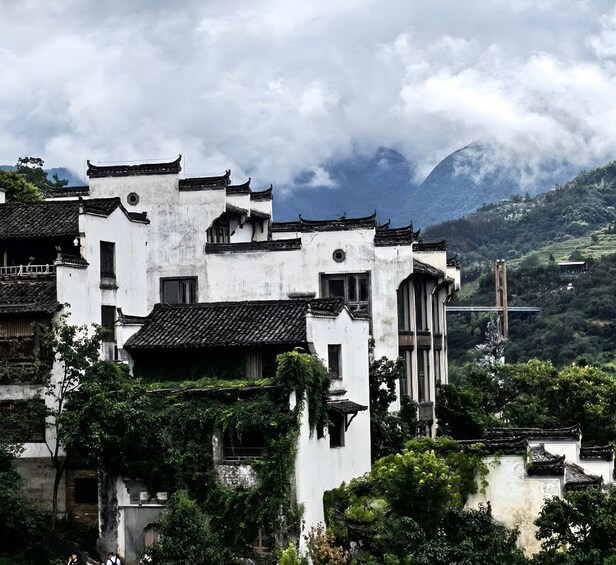 Des bâtiments blancs traditionnels aux toits noirs, entourés d’une végétation luxuriante et dominés par un paysage montagneux embrumé. 1