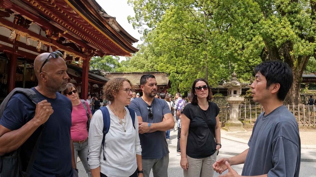 A group of tourists at a traditional Japanese temple with wooden architecture and a large tree in the background. 4