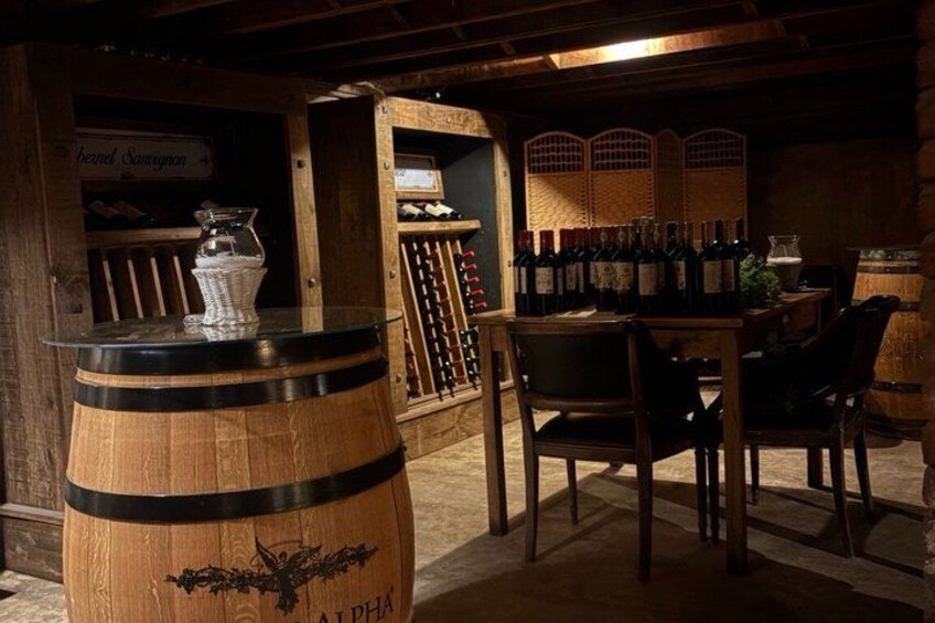 A wooden barrel with a label, a wine rack, and a table with chairs in a dimly lit room. 3