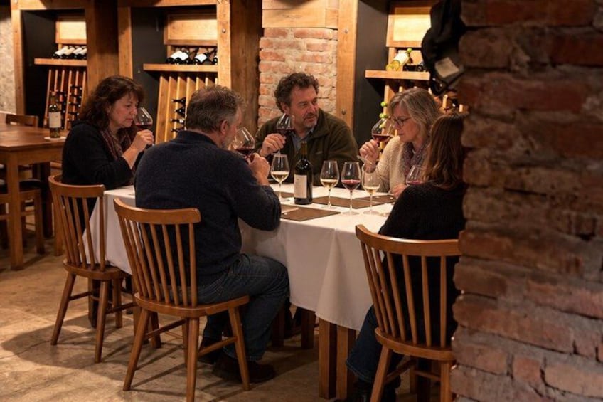 A group of people seated at a table in a rustic restaurant with wooden chairs and a brick wall in the background. 1
