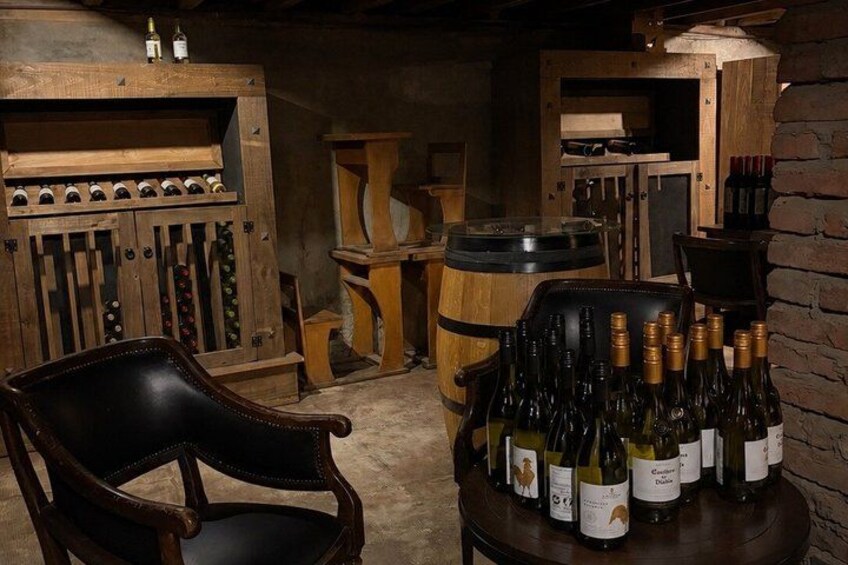 A wooden wine rack with bottles, a barrel, and a chair in a rustic cellar. 2