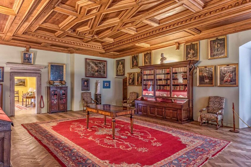 A room with wooden ceiling, bookshelves, framed pictures, and a red carpet. 4
