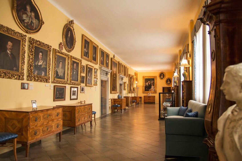 A room with a long wall of framed portraits, wooden furniture, and a statue. 5