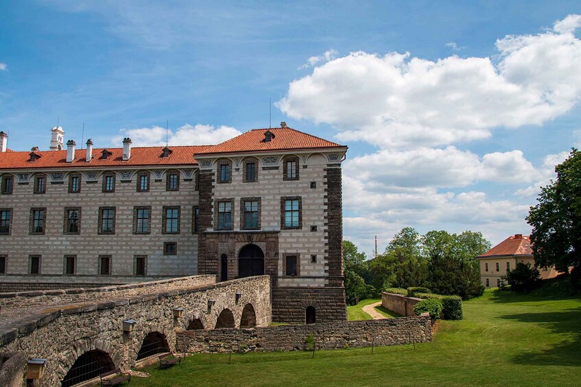 A large historic building with a red-tiled roof, stone walls, and a surrounding garden. 2