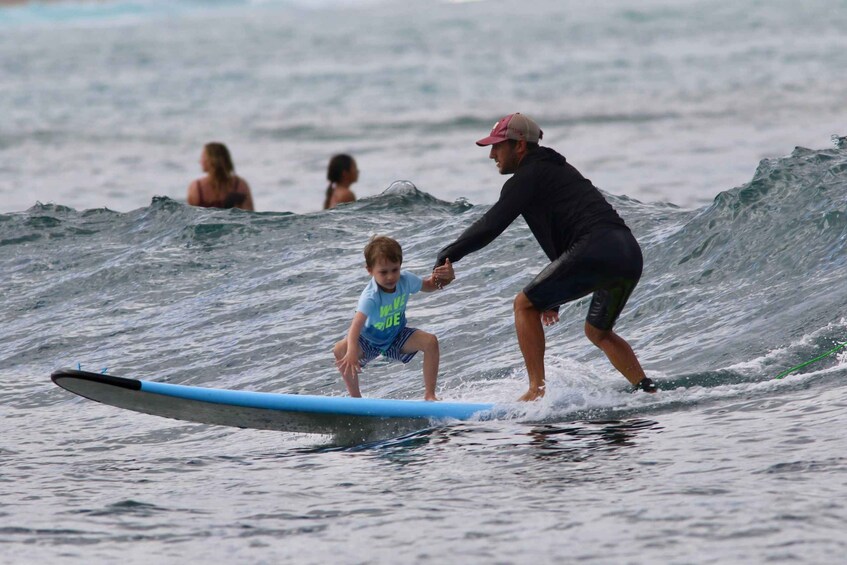 A person in a wetsuit assisting a child on a blue surfboard in the ocean. 4