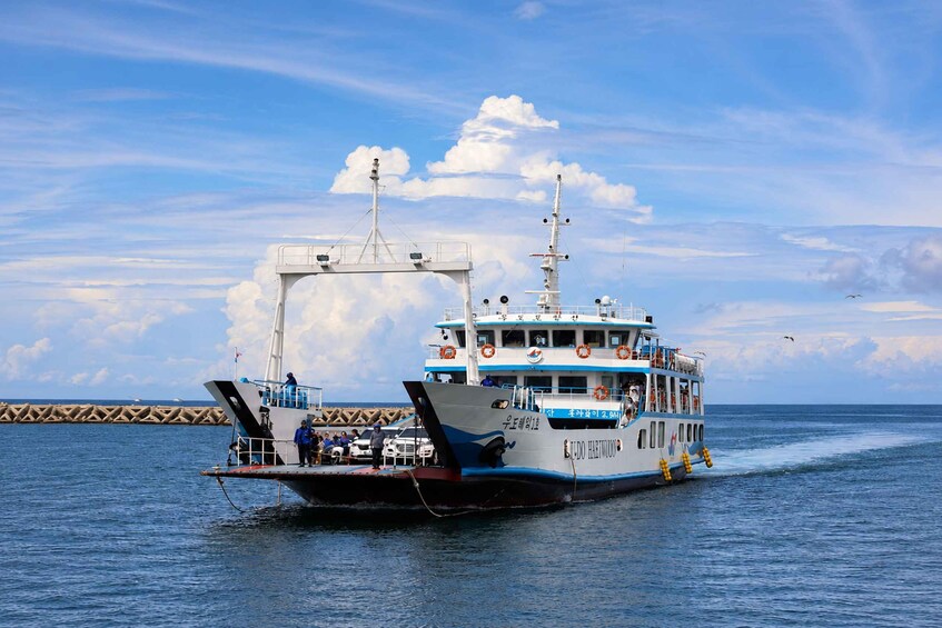 Un ferry con pasajeros y vehículos a bordo, navegando sobre una masa de agua con cielo despejado y nubes al fondo. 5