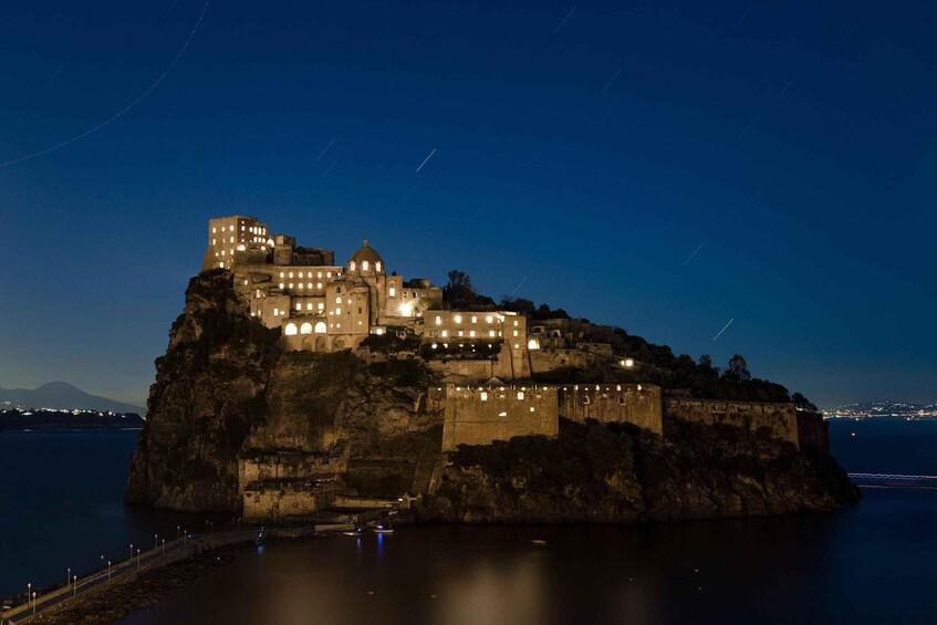 A historic fortified castle on a rocky island with illuminated windows, overlooking a calm body of water. 3