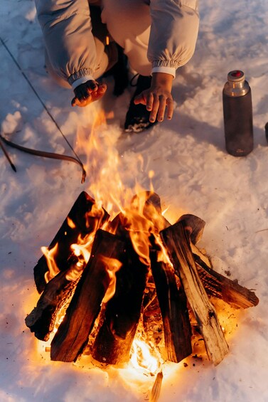 A person tending to a campfire in a snowy environment. 4