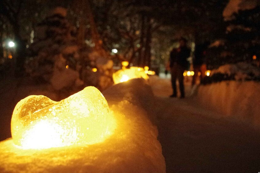 A snow-covered landscape with a glowing ice sculpture in the foreground and a person standing in the background. 2