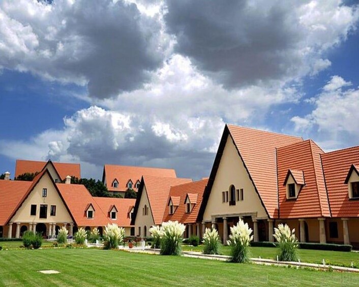 Une rangée de bâtiments traditionnels aux toits rouges et aux murs de couleur beige, entourés d’une pelouse bien entretenue et de plantes en fleurs. 2