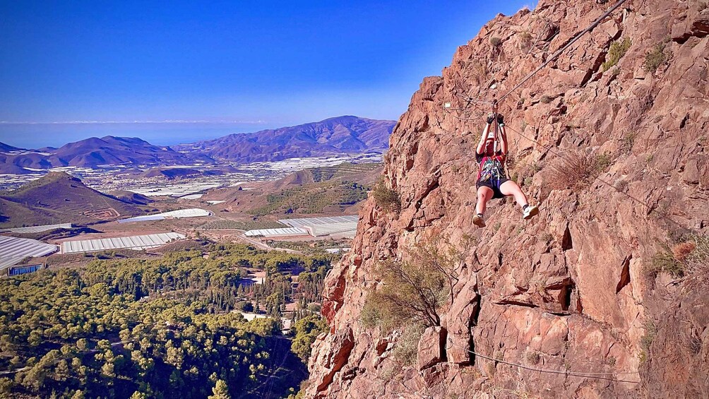 A person rock climbing on a steep cliff with a city and mountains in the background. 2