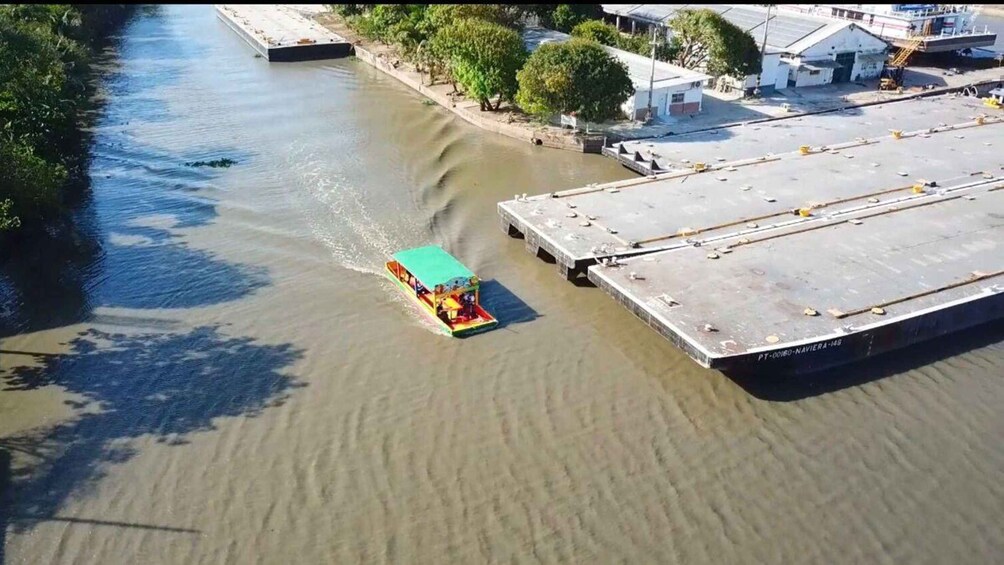 Una embarcación de colores navegando por un río cerca de un edificio industrial grande. 1