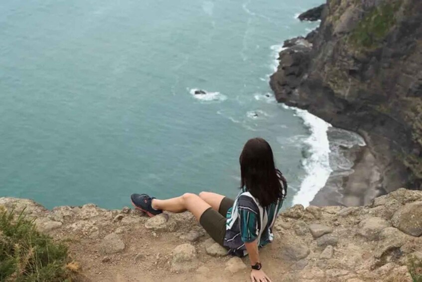 Una persona sentada en un risco rocoso con vista a una masa de agua y olas rompiendo en la orilla. 1