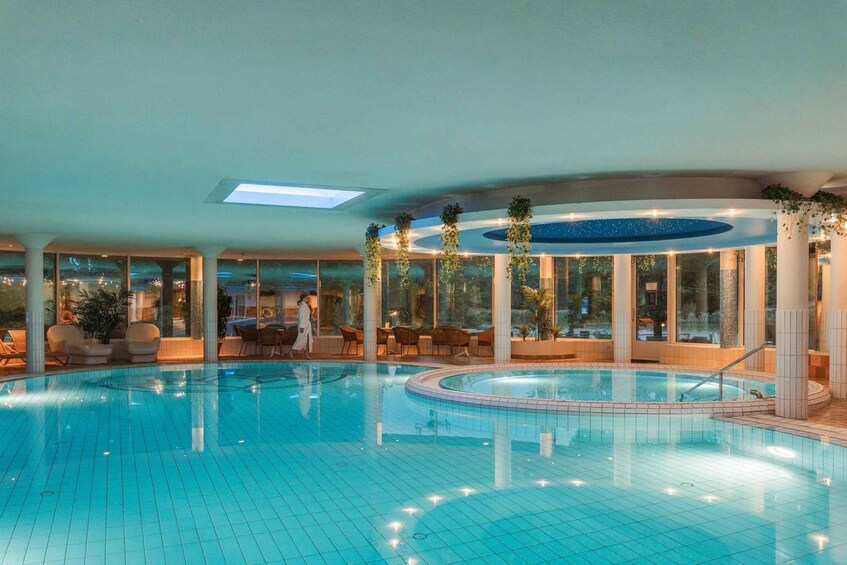 An indoor swimming pool with tiled flooring, a central hot tub, and surrounding seating areas. 3