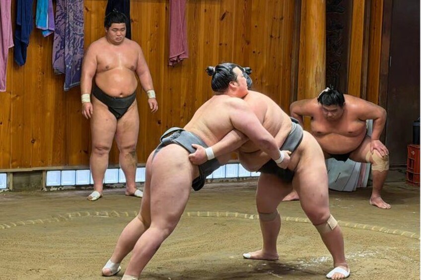 Two sumo wrestlers in a ring, one in a defensive stance, the other in a fighting stance. 4