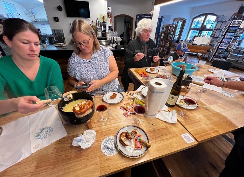 Un grupo de personas cenando en una mesa de madera con varios platos, copas de vino y una botella. 2