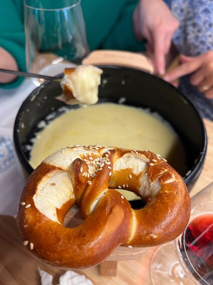 Un pretzel con semillas de sésamo, un tazón de sopa y una copa de vino tinto. 1