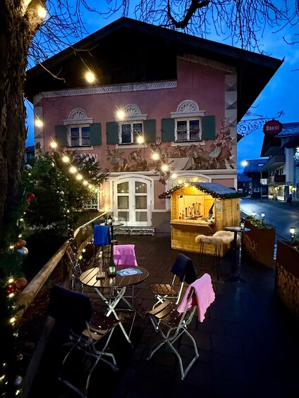 Un área de estar al aire libre con decoración festiva, luces colgantes, un árbol de Navidad y un edificio con un mural. 4