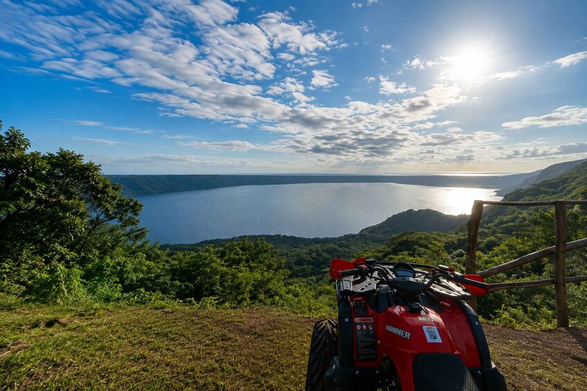A red ATV parked on a grassy hill overlooking a calm lake with a clear sky. 4