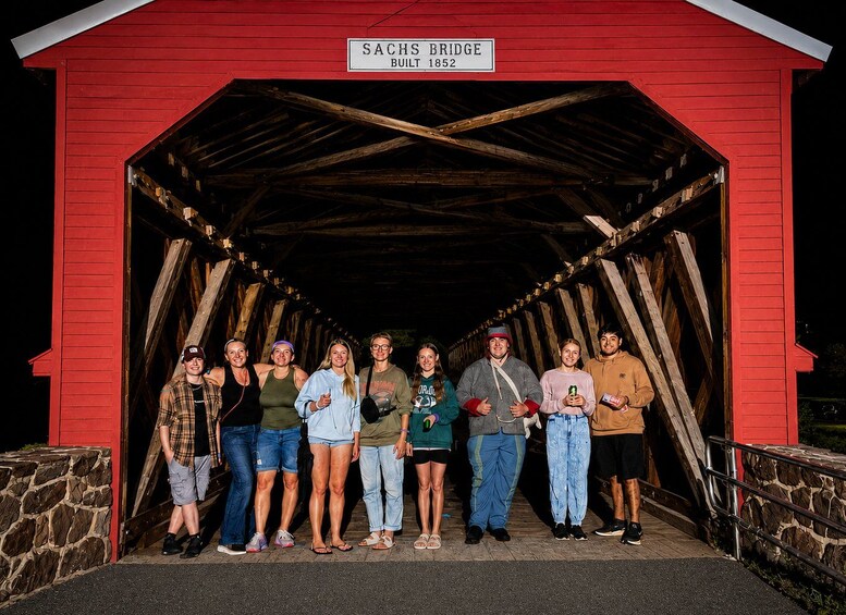 Un grupo de personas frente a un puente cubierto rojo con un letrero que dice 'SACHS BRIDGE BUILT 1852'. 2
