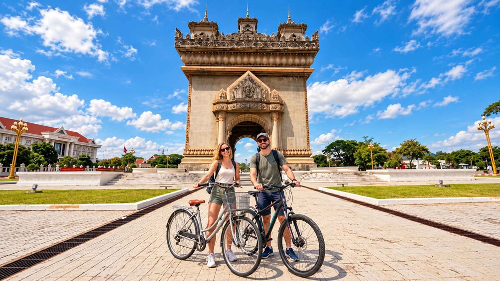 Un arco histórico con intrincados adornos, un camino empedrado y un edificio con techo rojo al fondo. 4