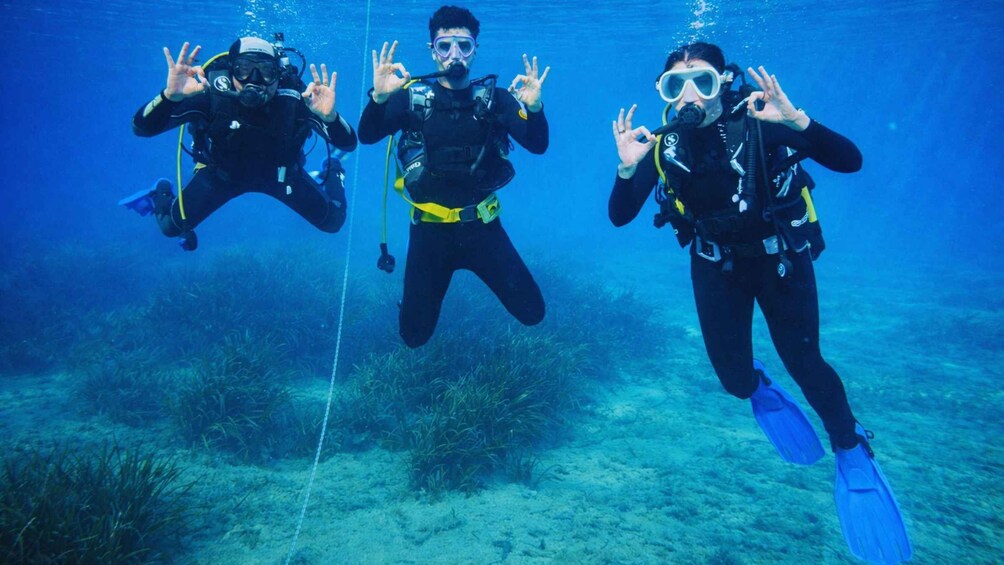 Three scuba divers underwater with fins and scuba gear, making hand gestures. 5