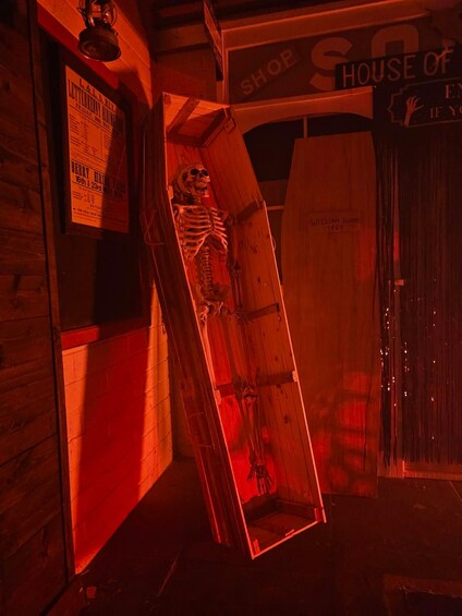 A skeleton in a wooden coffin in a dimly lit room with a sign that reads 'House of the Dead.' 3