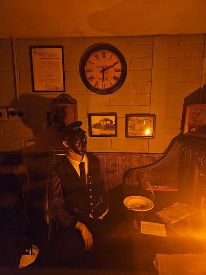 A vintage train station interior with a clock, framed pictures, and a person in uniform. 4