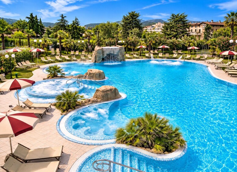 A large outdoor swimming pool with multiple hot tubs, surrounded by palm trees and lounge chairs. 2