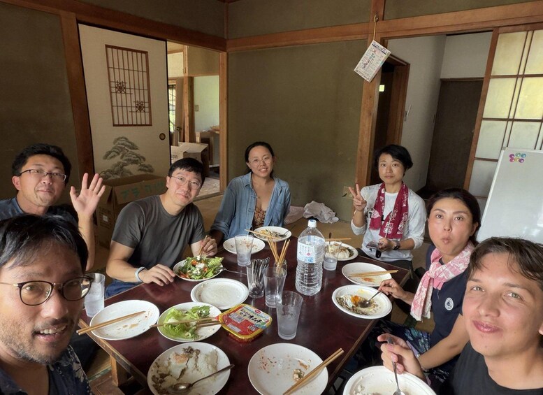 A group of people sitting around a wooden table with various dishes, including rice and vegetables, in a room with traditional Japanese sliding doors and a whiteboard. 4