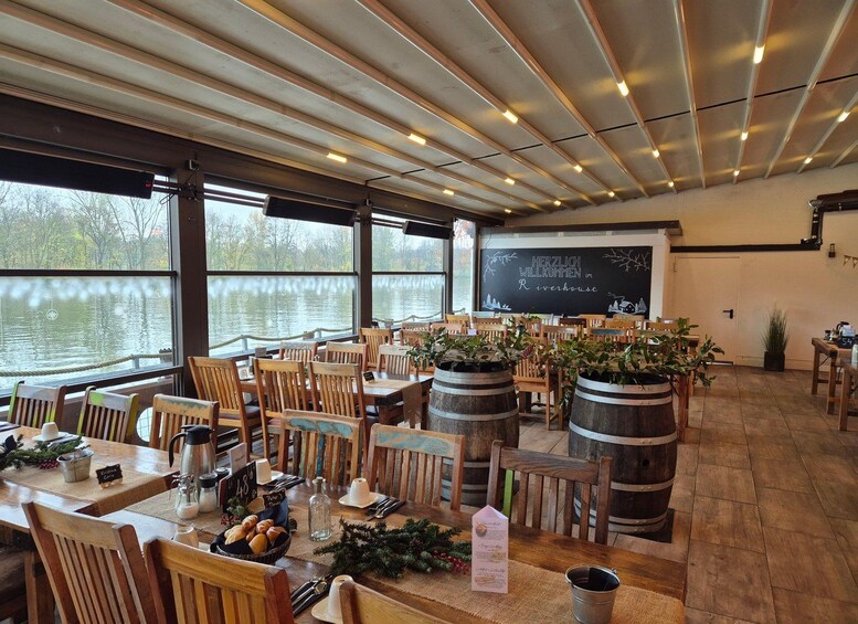 A restaurant with wooden tables and chairs, barrels, and a view of a lake. 4