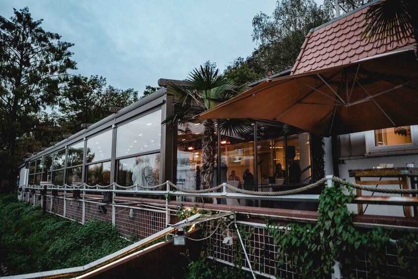 A glass-walled restaurant with outdoor seating, surrounded by greenery and a rope barrier. 2
