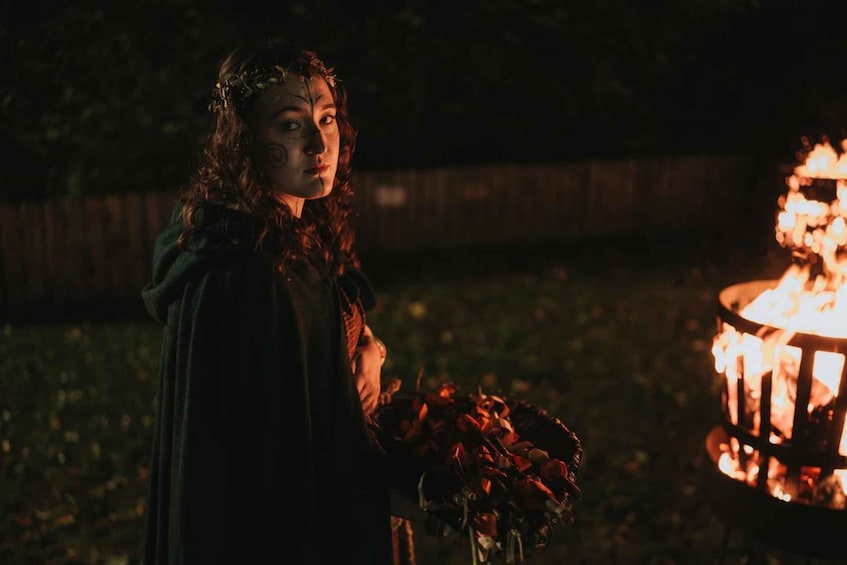 A person holding flowers near a lit fire pit at night. 1