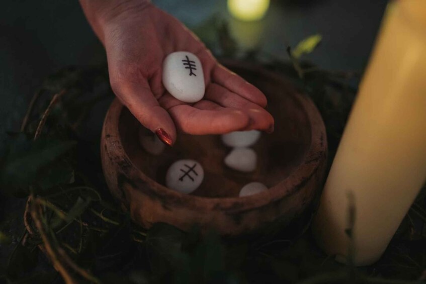 A hand holding a white object with a black symbol, over a wooden bowl with other similar objects. 3