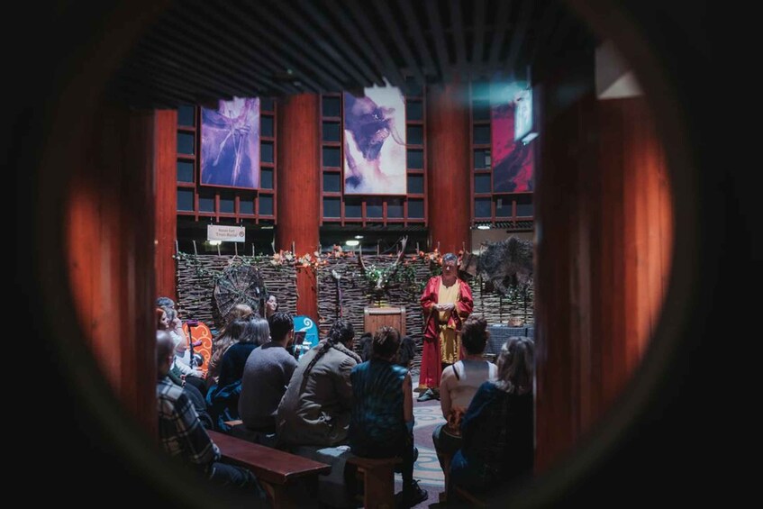 An outdoor event with a speaker on stage, an audience seated, and banners on the building. 2