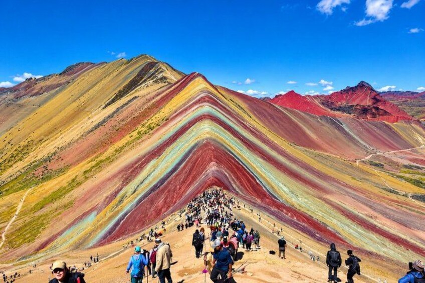 A colorful mountain landscape with a crowd of people at the base. 1