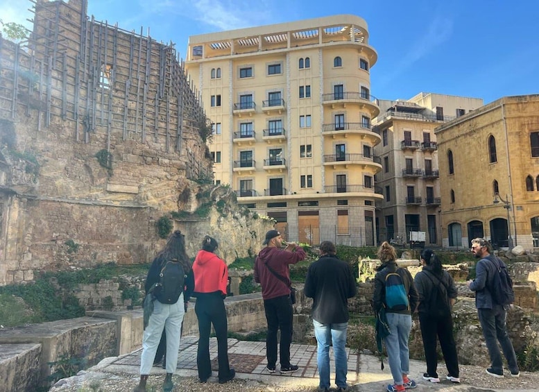 A group of people standing on a stone pathway in front of a building with a curved facade and a stone wall with scaffolding on the left. 3