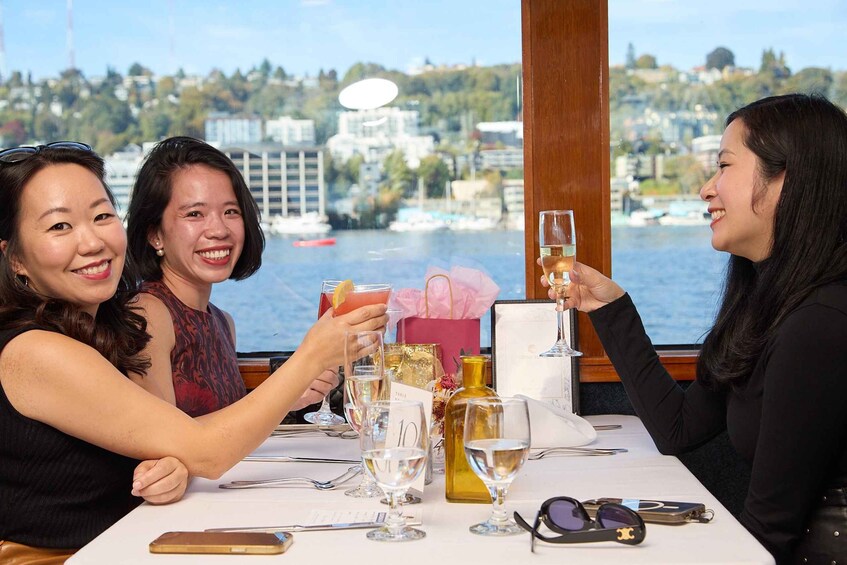 Three people toasting at a table with drinks and a scenic waterfront view. 4