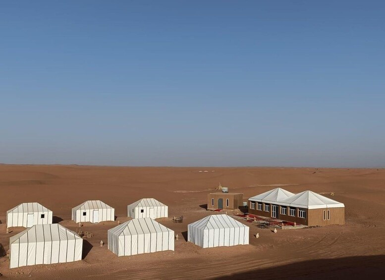 Un paysage désertique avec plusieurs tentes blanches et un seul bâtiment doté d’un toit plat. 2