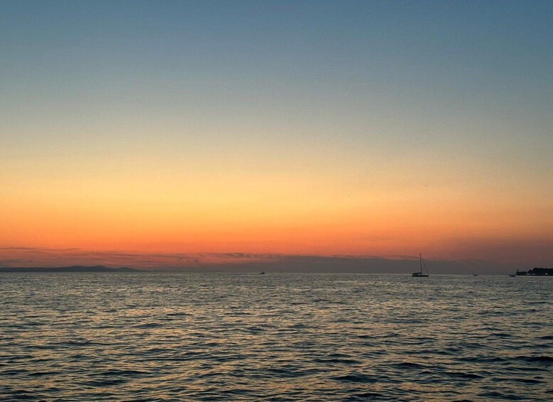 A sunset over a calm sea with a sailboat and distant land. 5