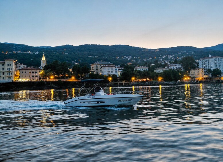 A boat named 'REVT A BOAT' with the number '280649 OP' on the water, a town with buildings and a hill in the background, and lights reflecting on the water. 1