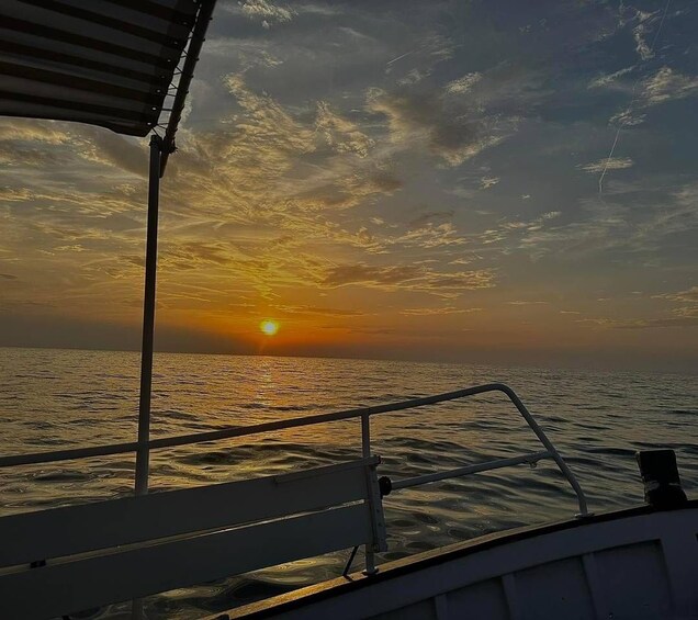 A boat at sunset with the sun near the horizon, a railing, and the ocean. 4