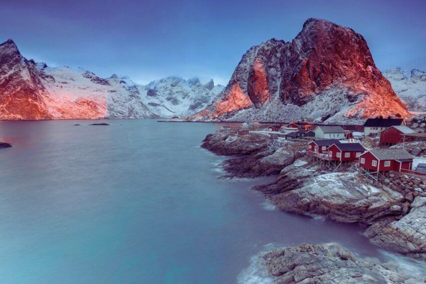 A fjord with red houses, a large mountain, and a calm sea. 4