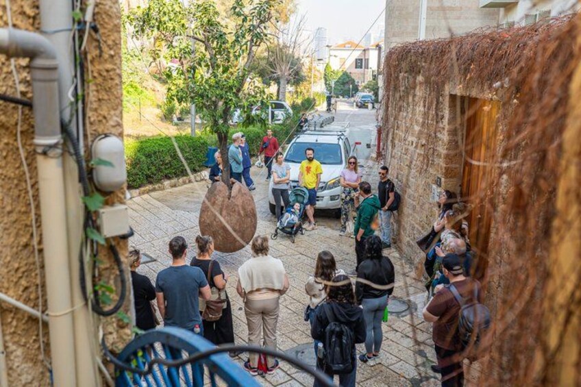 A group of people gathered on a street, some standing and some sitting, with a car parked in the background. 4