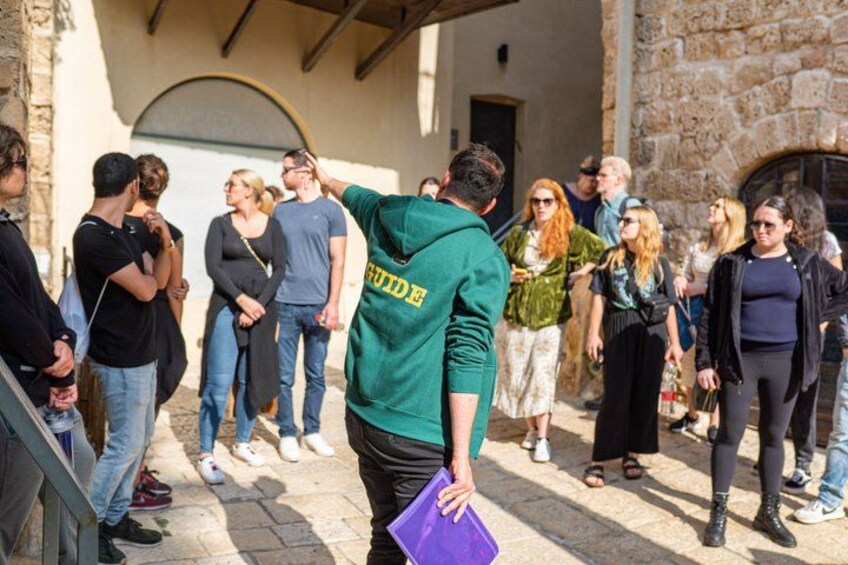 A group of people standing outdoors, some holding drinks, in a stone building with a rustic appearance. 3
