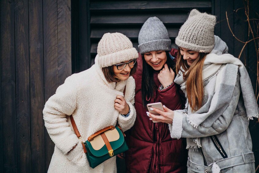 Three people wearing winter hats and jackets, one holding a phone. 3