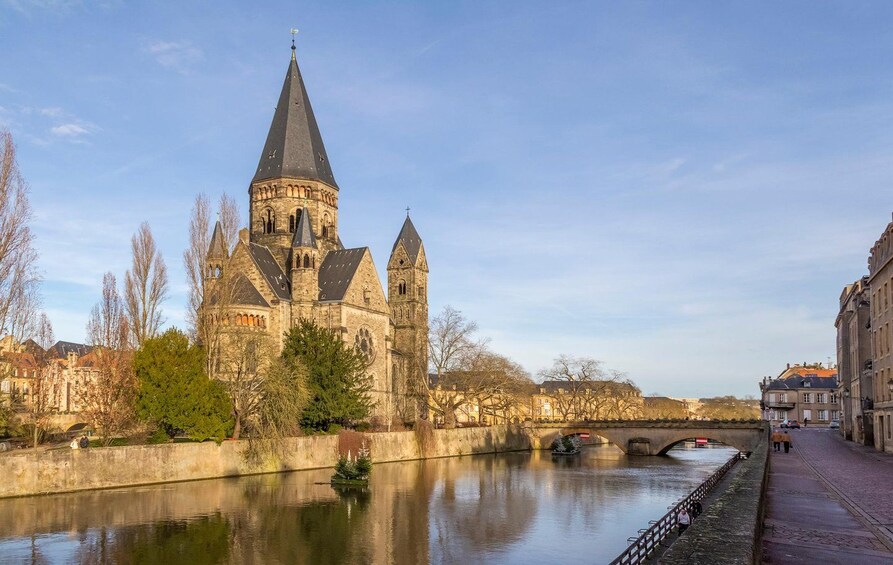 A historic church with a tall spire, a river, and a bridge. 1