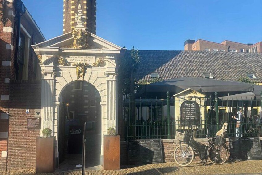 A historic building with an ornate entrance, a bicycle, and a covered area with a sign. 5