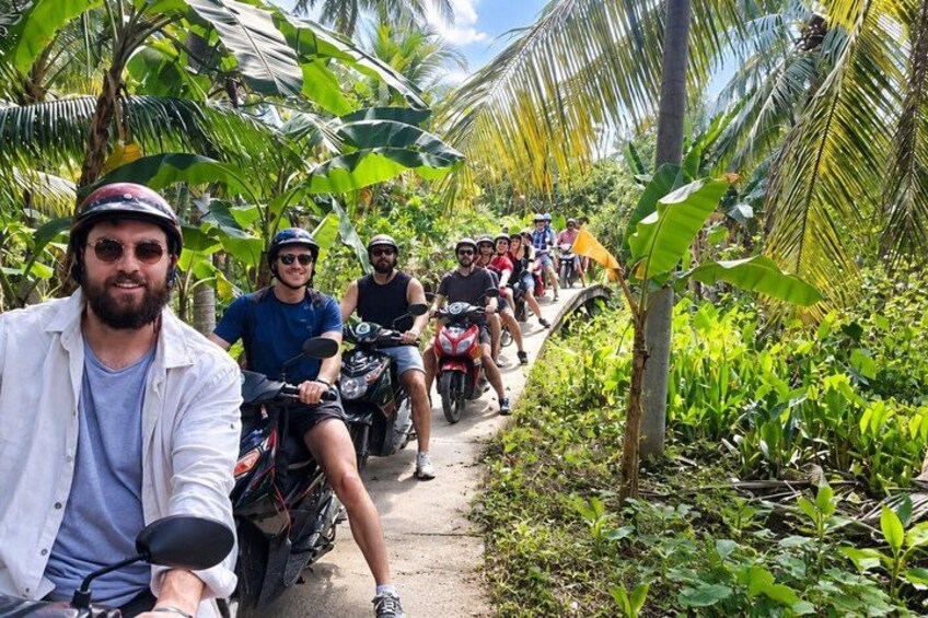 A group of people on motorcycles on a narrow path surrounded by lush greenery. 1