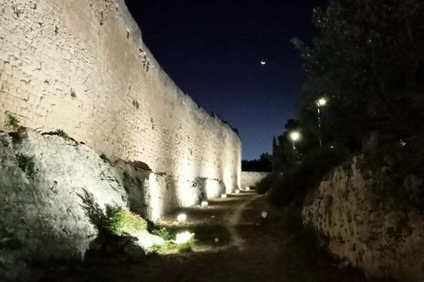 A stone wall with a narrow path leading through it, illuminated by street lamps. 2